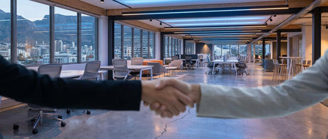 Two businesspeople shake hands in a modern office furniture showroom, with a subtle crack in the floor symbolising tension in the manufacturer-dealer relationship.